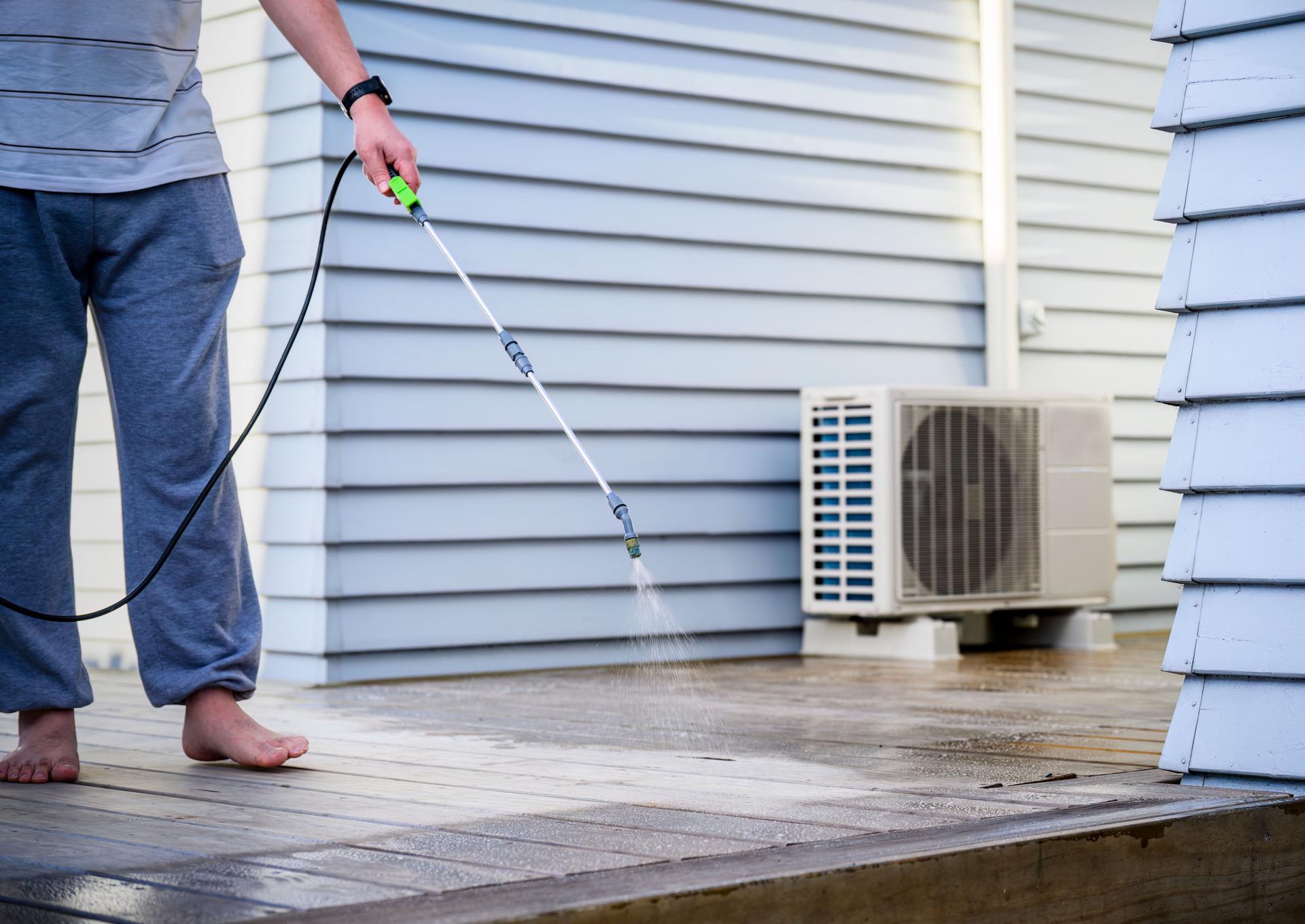 Man cleaning wooden deck with hand-held pressure sprayer, preparing deck before staining.